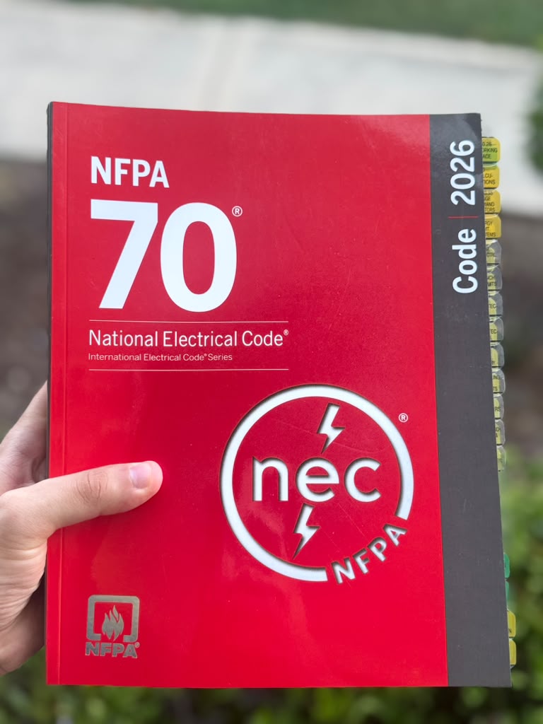 NEC 2026 codebook with handwritten exam notes from a Master Electrician